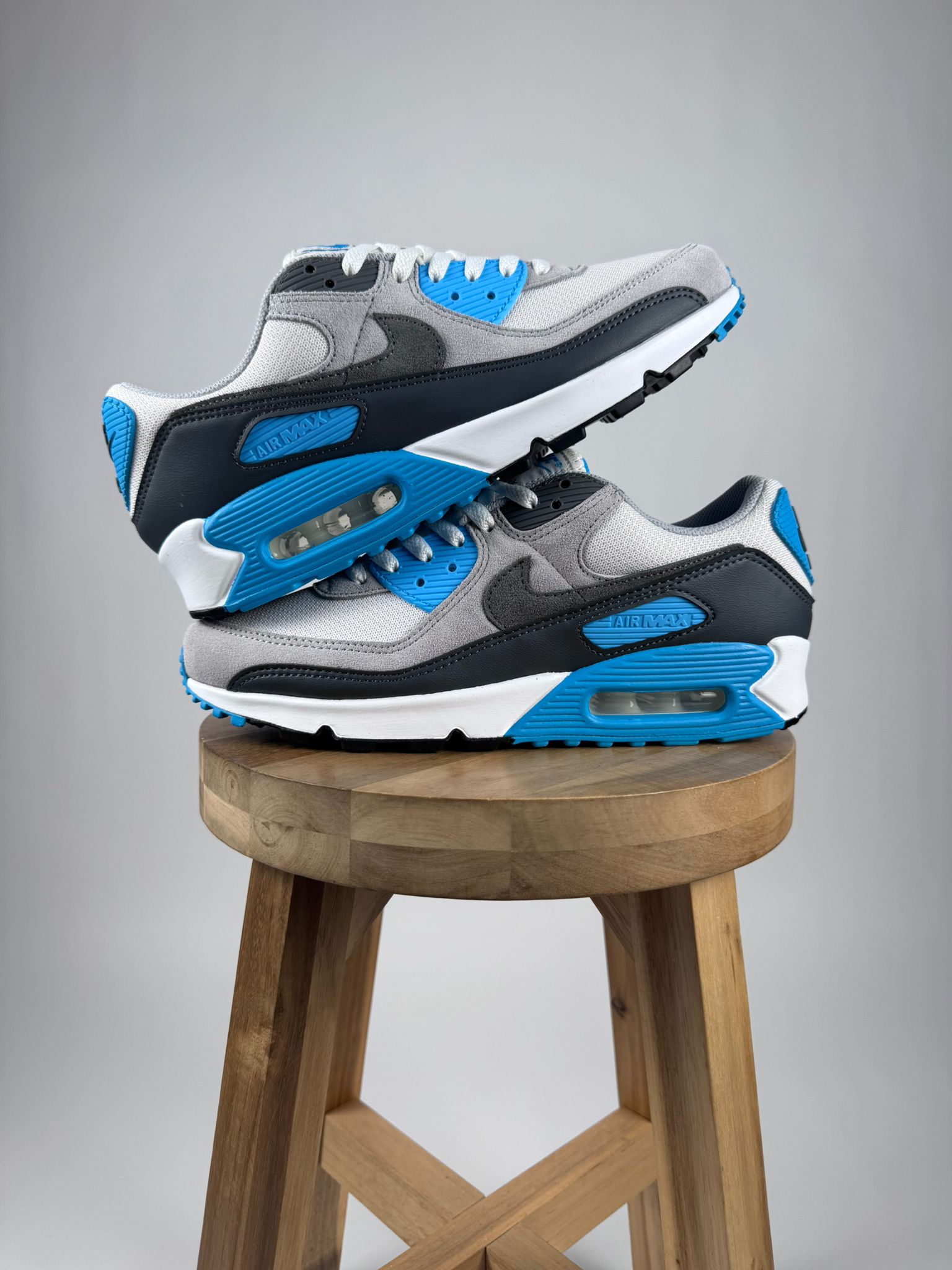 De Nike Air Max 90 Platinum Tint Blue Lightning opgestapeld op een krukje zij aanzicht